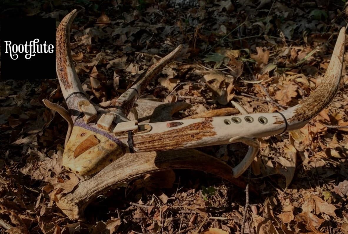 A handcrafted antler flute with both curved antler ends visible, resting on the forest floor